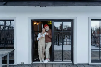An older man handing a set of house keys to a younger woman at the front door of a residential home.