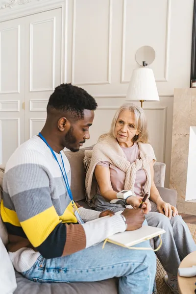 A care manager sitting at a kitchen table reviewing notes with an older woman