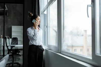 An adult child on a video call with an older parent, sitting at a desk with paperwork and a laptop.