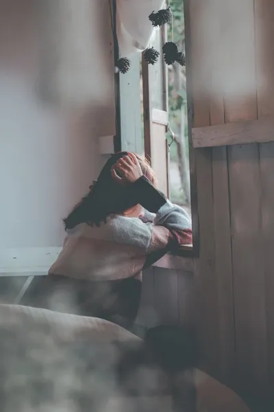 A woman sitting on a front porch at dusk, looking out at a quiet street, a mug in her hands