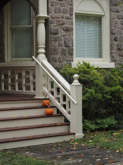 A stately residential home on a tree-lined street in a New York suburb with a wide front porch and autumn foliage.
