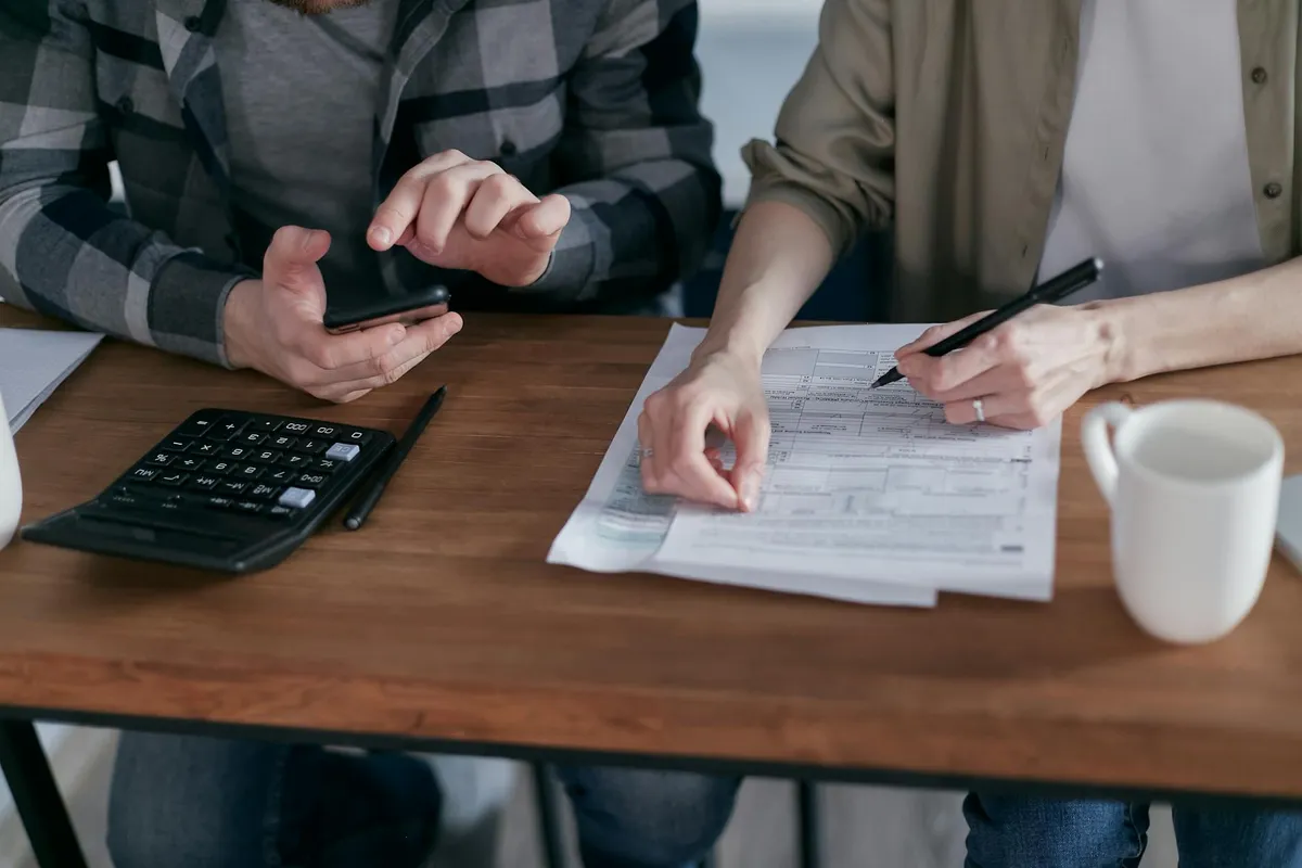 An older couple at a kitchen table reviewing financial paperwork together with a calculator and a cup of coffee.