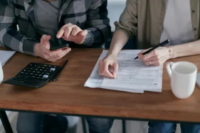 An older couple at a kitchen table reviewing financial paperwork together with a calculator and a cup of coffee.