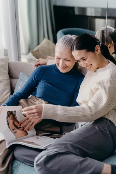A woman sitting next to her elderly mother in a bright common room, holding her hand and looking at a photo album together