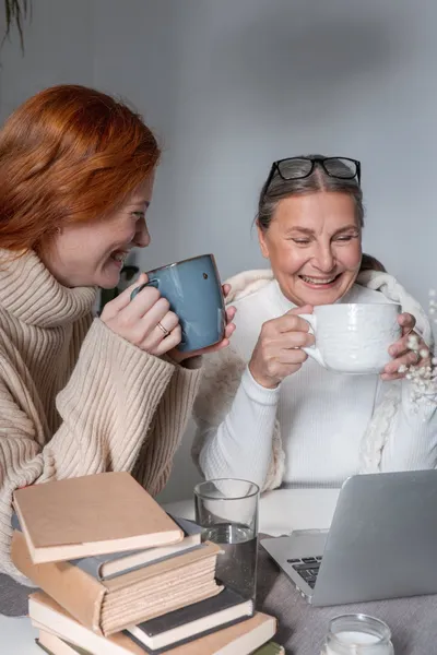 An adult daughter sitting at a kitchen table with her elderly father, a cup of coffee between them, afternoon light through the window