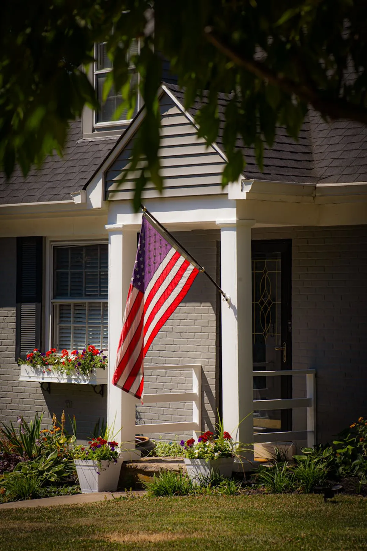An older veteran in a cardigan holding a folded American flag, seated in a sunlit living room.