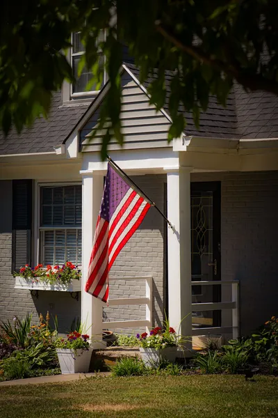 An older veteran in a cardigan holding a folded American flag, seated in a sunlit living room.
