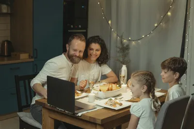 A laptop open on a kitchen table showing a video call, with a cup of tea beside it.